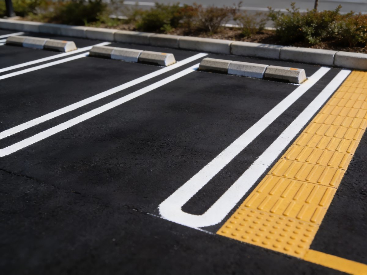 Freshly painted white parking stall lines on deep black asphalt with concrete wheel stops and a yellow accessible edge strip